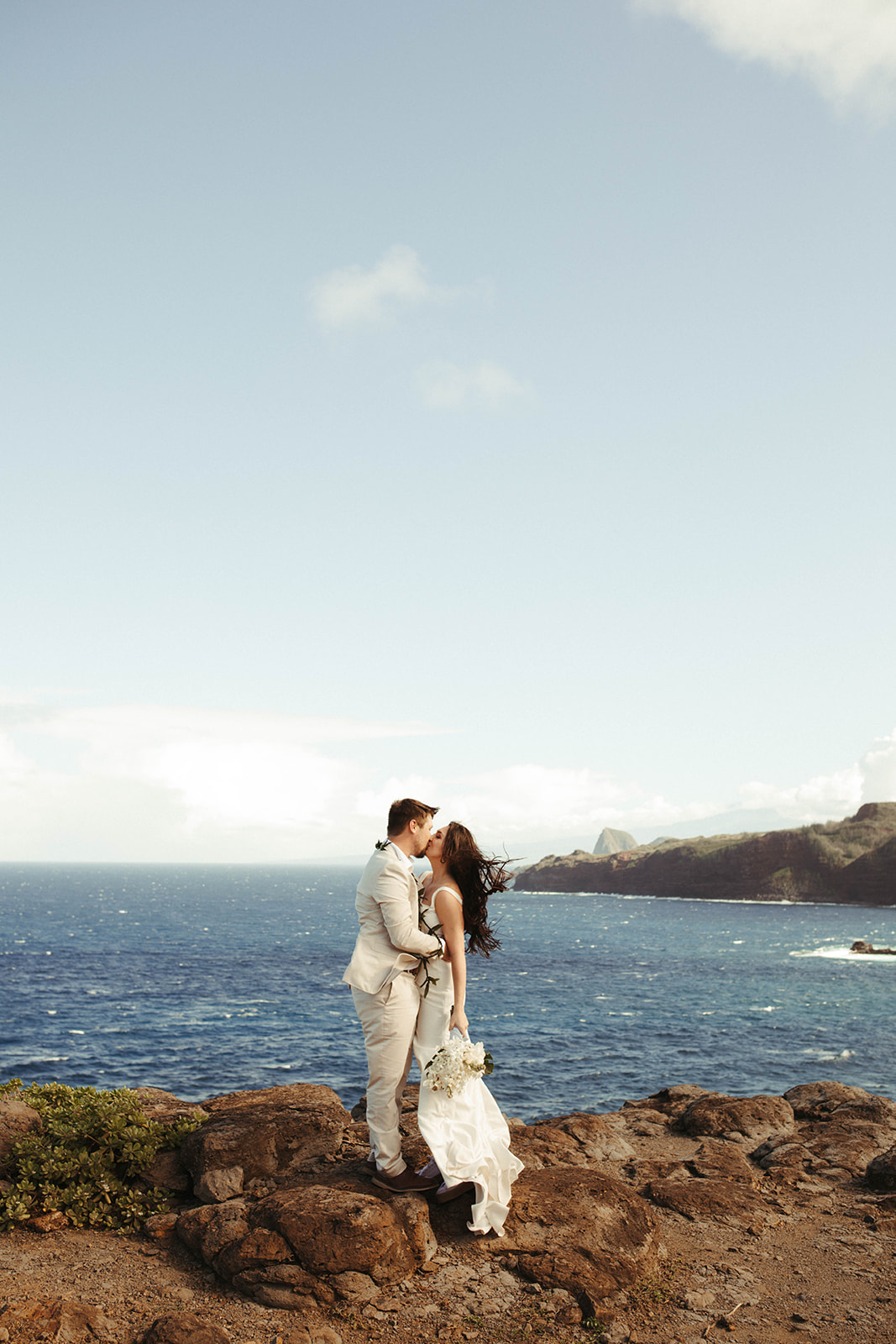 bride and groom kissing on a cliffside in maui, hawaii